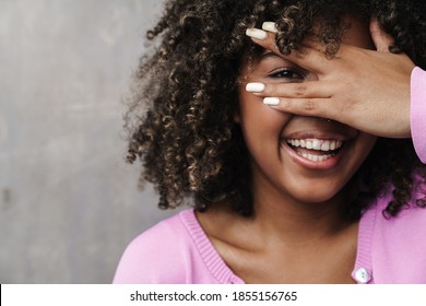 Cheerful African American Woman Peeking And Covering Her Face Isolated Over Grey Wall