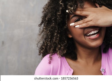 Cheerful African American Woman Peeking And Covering Her Face Isolated Over Grey Wall