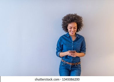 Cheerful African American Woman Standing Isolated Over Gray Background, Holding Mobile Phone. Smiling Lovely Young Woman Standing And Using Cell Phone Over Grey Background 