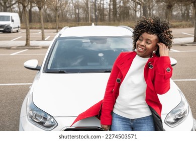 a cheerful african american woman stands next to the White car and laughing