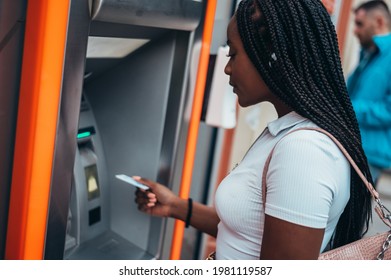 Cheerful african american woman using credit card and withdrawing cash at the ATM