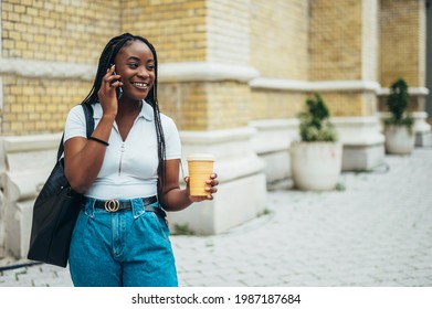 Cheerful african american woman using smartphone and drinking coffee takeaway while out in the city