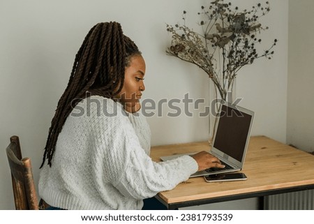 Cheerful african american woman using laptop while sitting on chair in living room - student, video call and working at home concept