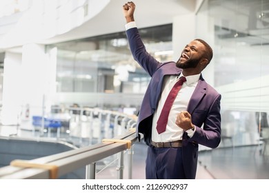 Cheerful african american young businessman celebrating success, handsome black manager in suit and tie raising hands up and screaming, office building interior, panorama with copy space - Shutterstock ID 2126902937