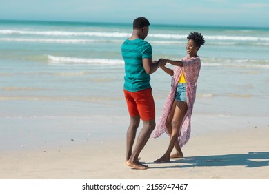 Cheerful african american young couple holding hands and dancing at beach against sky on sunny day. nature, summer, happy, unaltered, beach, love, togetherness, lifestyle, enjoyment and holiday. - Powered by Shutterstock