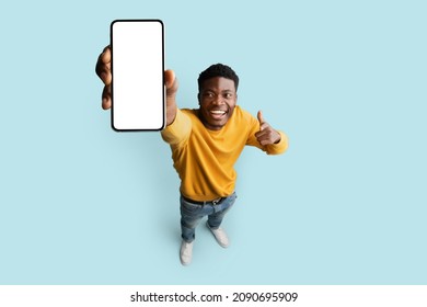 Cheerful african american young man in yellow showing modern cellphone with blank white screen and smiling on blue studio background, mockup, recommending newest mobile app, top view, copy space - Shutterstock ID 2090695909