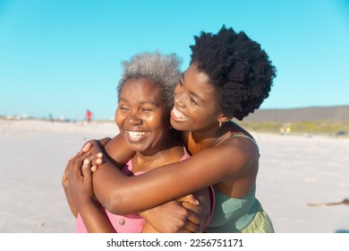 Cheerful african american young woman embracing senior mother and enjoying at beach against blue sky. Copy space, unaltered, family, summer, together, vacation, retirement, afro hair, nature. - Powered by Shutterstock