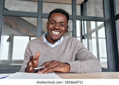 Cheerful african business man talking to web cam on conference call. Happy black businessman, coach, tutor wearing headset laughing, looking camera during webinar, online class, webcam view. Headshot