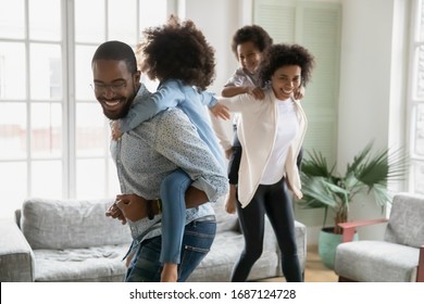 Cheerful African couple play with children running piggy back riding little kids celebrating moving day at new first modern home. Family have fun enjoy free time together leisure active games concept