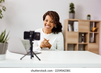 Cheerful African female employer talking online with clients, using a smartphone on a tripod. - Shutterstock ID 2259042381