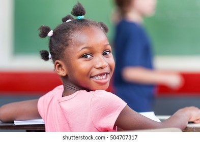 Cheerful African Girl Smiling In Primary Classroom.