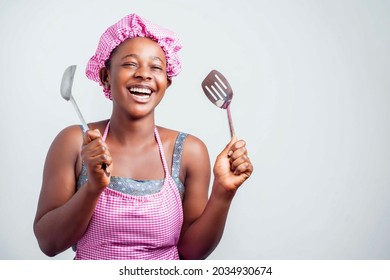 alegre dama africana sosteniendo artículos de cocina, chica negra en delantal y emoción por el envoltorio de la cabeza - concepto de comida interior