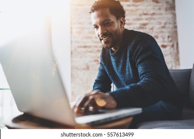 Cheerful African Man Using Computer And Smiling While Sitting On The Sofa.Concept Of Young Business People Working At Home.Blurred Background,flares