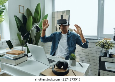 Cheerful African Man Wearing Virtual Reality Glasses While Sitting At Working Place