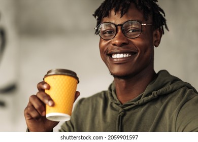 cheerful african man with a white paper cup in his hands, sitting in a cafe, smiling and looking at the camera. addicted to coffee or tea. aroma of coffee - Powered by Shutterstock