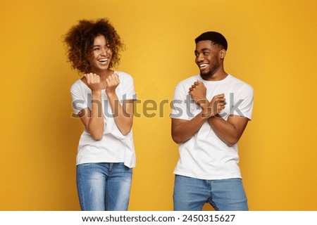 Cheerful african man and woman fooling, clenching fists on orange background