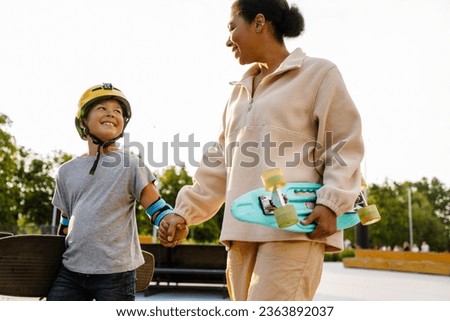 Cheerful african mother and her son with skateboards spending time together in summer park