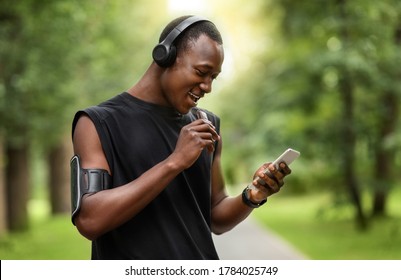 Cheerful African Sportsman Eating Protein Bar And Using Smartphone While Resting, Exercising At Park, Empty Space