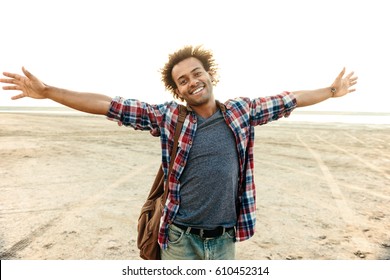 Cheerful african young man with arms spread opened standing at the beach