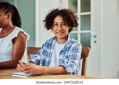 A cheerful African-American boy with curly hair sitting at the wooden table with a notebook, smiling for the camera. - Powered by Shutterstock