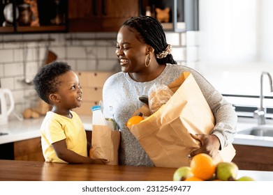 Cheerful African-American mother and son in the kitchen. Son helps a mother to bring in a groceries after a grocery-shopping - Powered by Shutterstock