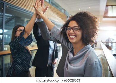 Cheerful African-American office worker giving high five to colleagues and looking at camera.