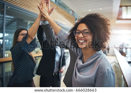Cheerful African-American office worker giving high five to colleagues and looking at camera.