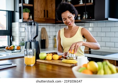 Cheerful African-American woman preparing healthy fruit drink after exercising at home