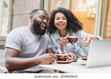 Cheerful african-american young romantic couple friends watching movie comedy online together,drinking coffee in city cafe, surfing Internet, social media, watching webinar online outdoors