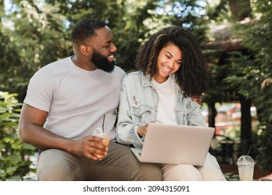 Cheerful african-american young romantic couple friends watching movie comedy online together, surfing Internet, social media, watching webinar online outdoors in city park - Powered by Shutterstock