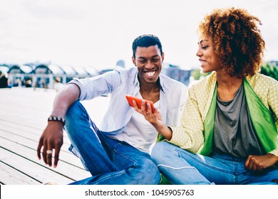 Cheerful Afro American Guy Smiling While Reading News About Sales In Web Store On Girlfriend's Mobile,happy Couple In Love Having Fun Watching Videos On Smartphone While Resting Outdoors Together