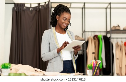 Cheerful Afro Fashion Designer Using Tablet Computer Browsing Internet In Dressmaking Studio. Empty Space - Powered by Shutterstock