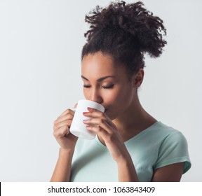 Cheerful Afro-American girl in casual clothes is drinking coffee or tea from a white cup, isolated on white - Powered by Shutterstock