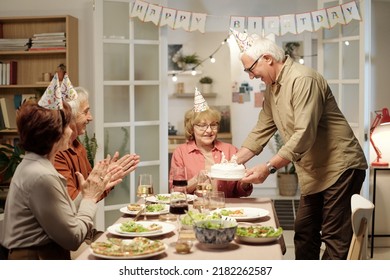 Cheerful Aged Man In Cap Putting Delicious Birthday Cake On Served Festive Table During Celebration Of Life Event At Home Party