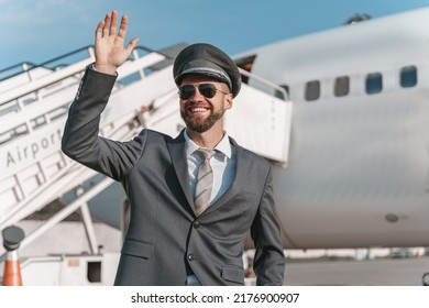 Cheerful Aircraft Pilot Standing Outdoors At Airport And Waving Hello To Colleagues