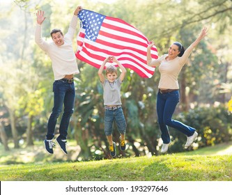 Cheerful American Family Jumping With USA Flag On 4th Of July