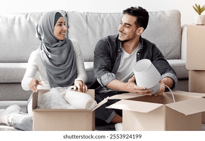 Cheerful arab family handsome husband and wife in hijab unpacking belongings and having conversation, dreaming about prosperous future, moving to new apartment or bought own house - Powered by Shutterstock