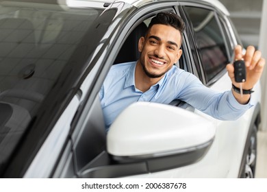 Cheerful Arab Man Holding Key From Auto, Buying Brand New Car In Showroom. Happy Middle-eastern Guy Buying New Automobile, Sitting Inside Black Car And Showing Automatic Key At Camera, Smiling