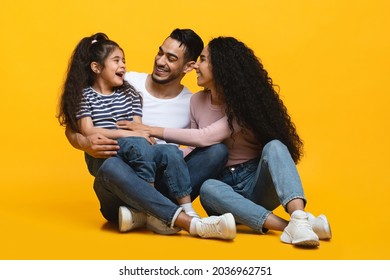 Cheerful Arab Parents Having Fun With Their Little Daughter Over Yellow Studio Background, Happy Playful Middle Eastern Mom And Dad Tickling Female Child And Laughing Together, Free Space