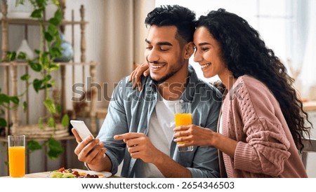 Cheerful Arab Spouses Using Smartphone While Eating Breakfast In Kitchen