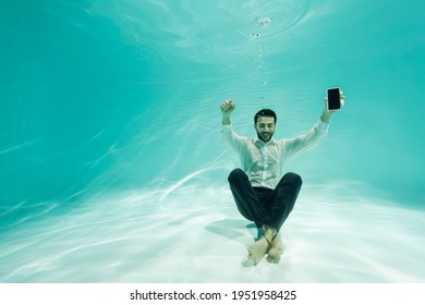 Cheerful arabian businessman with smartphone showing yes gesture underwater - Powered by Shutterstock