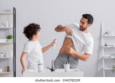 Cheerful Arabian Man Lifting T-shirt Near Son With Deodorant