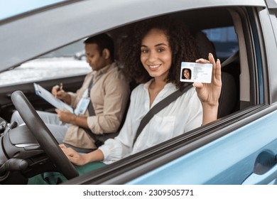 Cheerful Arabic Novice Driver Lady Showing Driving License Card Through Open Automobile Window, Sitting Beside Instructor Man In Car. Woman Got Her Driver's Permit Concept. Selective Focus - Shutterstock ID 2309505771
