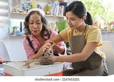 Cheerful Asian Aged Woman Potter Teacher Teaching And Coaching A Beautiful Young Student To Make A Ceramic Bowl On Potter's Wheel.