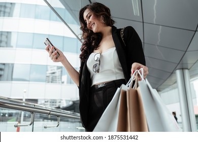 Cheerful asian businesswoman shopping in the city, holding smartphone.