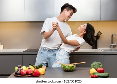 Cheerful Asian Couple Cooking And Dancing Having Fun While Preparing Dinner Together In Modern Kitchen, Having Romantic Date At Home. Family Weekend Leisure, Food Preparation Concept