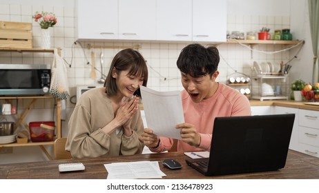 cheerful Asian couple happy while making budget plan at home. man screams with raised fist as woman applauds and pointing at computer, happy about being able to afford dream house