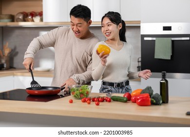 Cheerful Asian Couple Middle Aged Husband And Young Wife Enjoying Cooking Together At Home, Happy Chinese Man And Woman Standing Next To Stove, Preparing Healthy Dinner, Copy Space