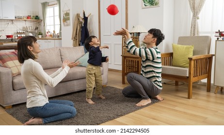 Cheerful Asian Dad, Mom And Preschool Son Enjoying Playing Together With A Red Balloon At Home. They Hit And Catch The Red Balloon To Prevent It From Falling On Floor