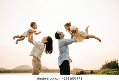 A cheerful Asian family enjoys a day out in nature, as the father and mother throw their toddler up into the sunny sky. The happy child enjoys the playful freedom of flying, captured in a photograph - Powered by Shutterstock